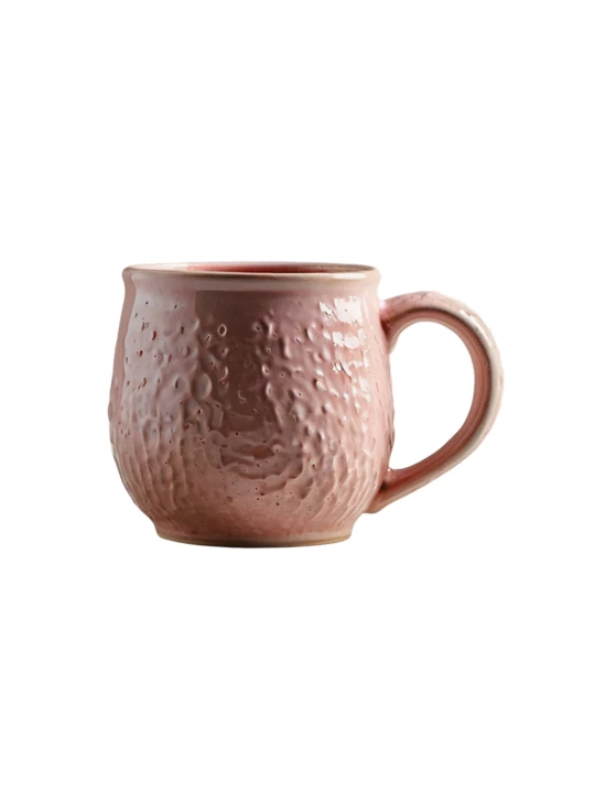 Różowy kubek ceramiczny o pękatym kształcie i zaokrąglonym uchu na jednolitym białym tle. Korpus ma mocno teksturowaną, wgłębioną powierzchnię przypominającą kratery, pokrytą błyszczącym szkliwem.